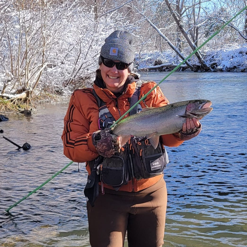 Smiling angler holding a large steelhead trout on a snowy riverbank, fishing with a green Wasatch Tenkara Rods SIYCO rod—showcasing the rod’s power and performance in cold-weather fly fishing conditions.