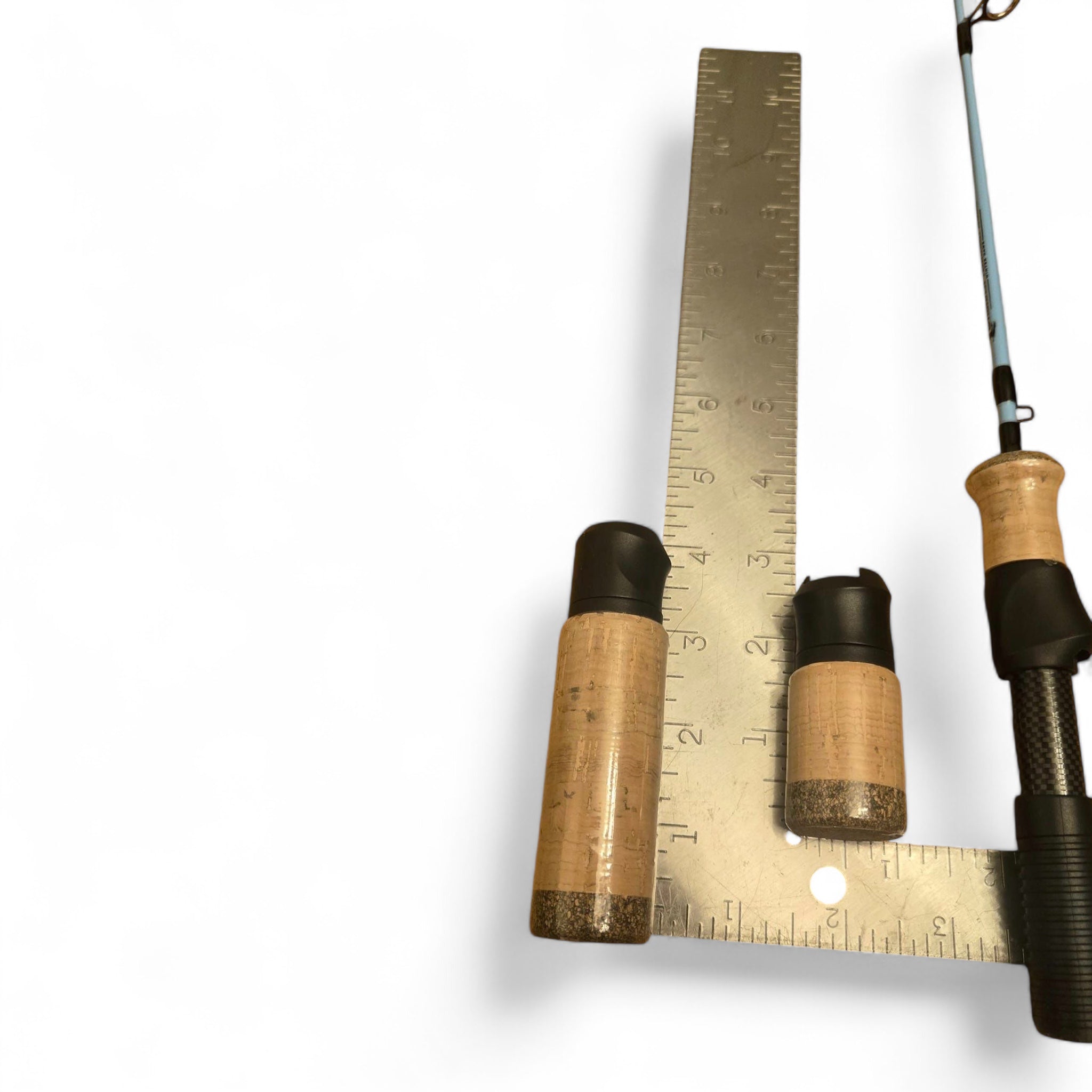 Two sizes of cork handles for a Wasatch Tenkara Rods - Winterhawk ice fishing rod placed beside a metal ruler for measurement, with part of the blue rod and carbon fiber section visible on a white background.